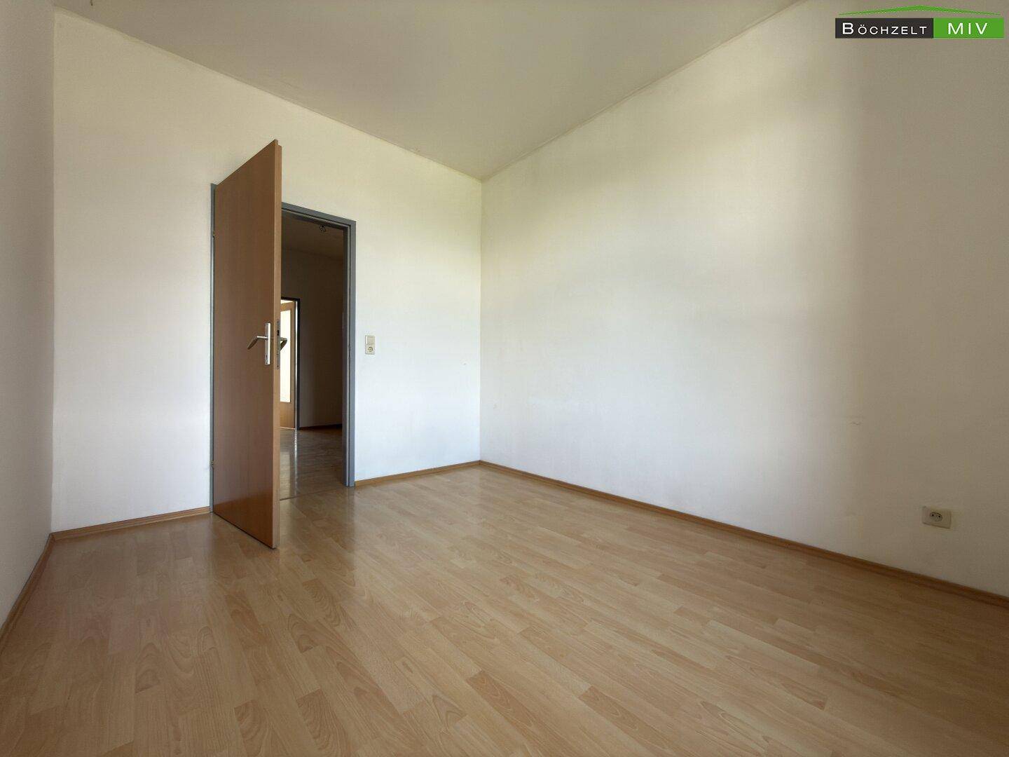 Leeres Zimmer mit Laminatboden und weißen Wänden, bereit zur individuellen Gestaltung.