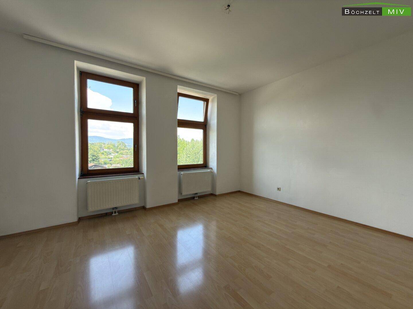Geräumiges Zimmer mit Laminatboden und zwei großen Fenstern, die viel Tageslicht hereinlassen.