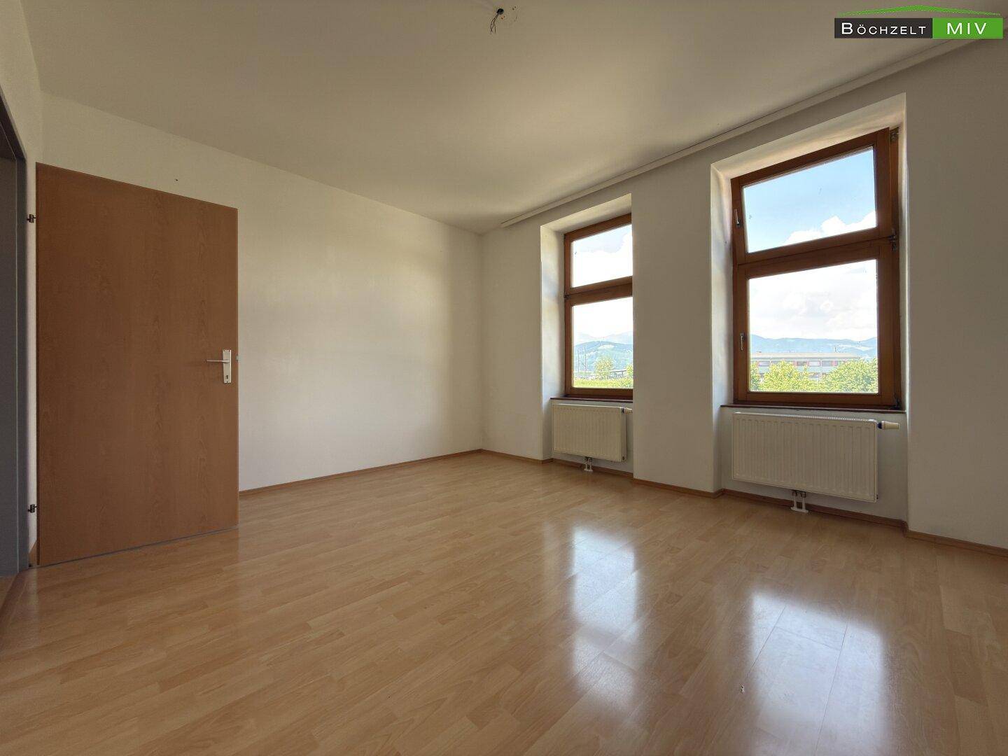 Helles Zimmer mit Laminatboden und zwei Fenstern, die einen weiten Blick in die Landschaft bieten.