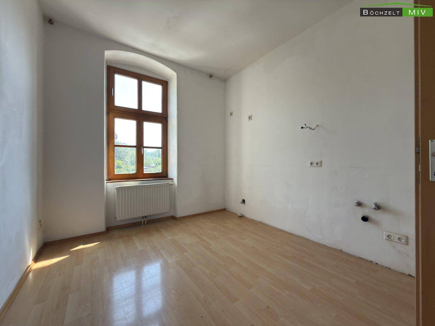 Leeres Zimmer mit Laminatboden und Anschlüssen für eine Küche oder ein Badezimmer.