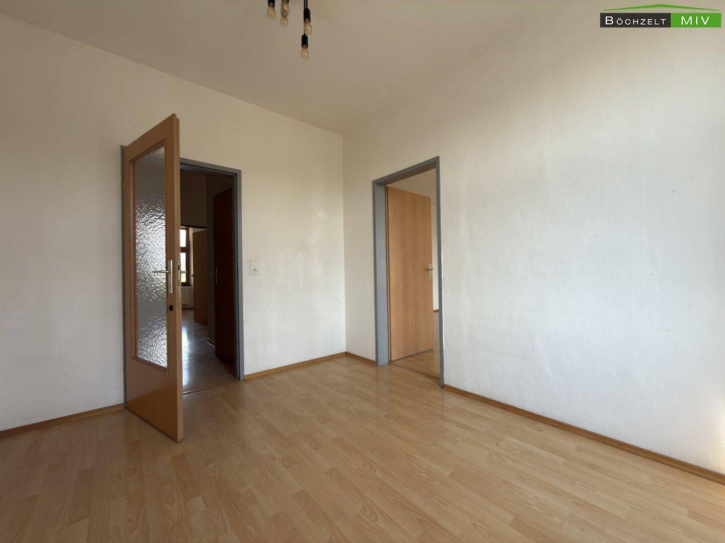 Helles Zimmer mit Laminatboden und zwei Türen, das als Wohn- oder Essbereich dienen könnte.