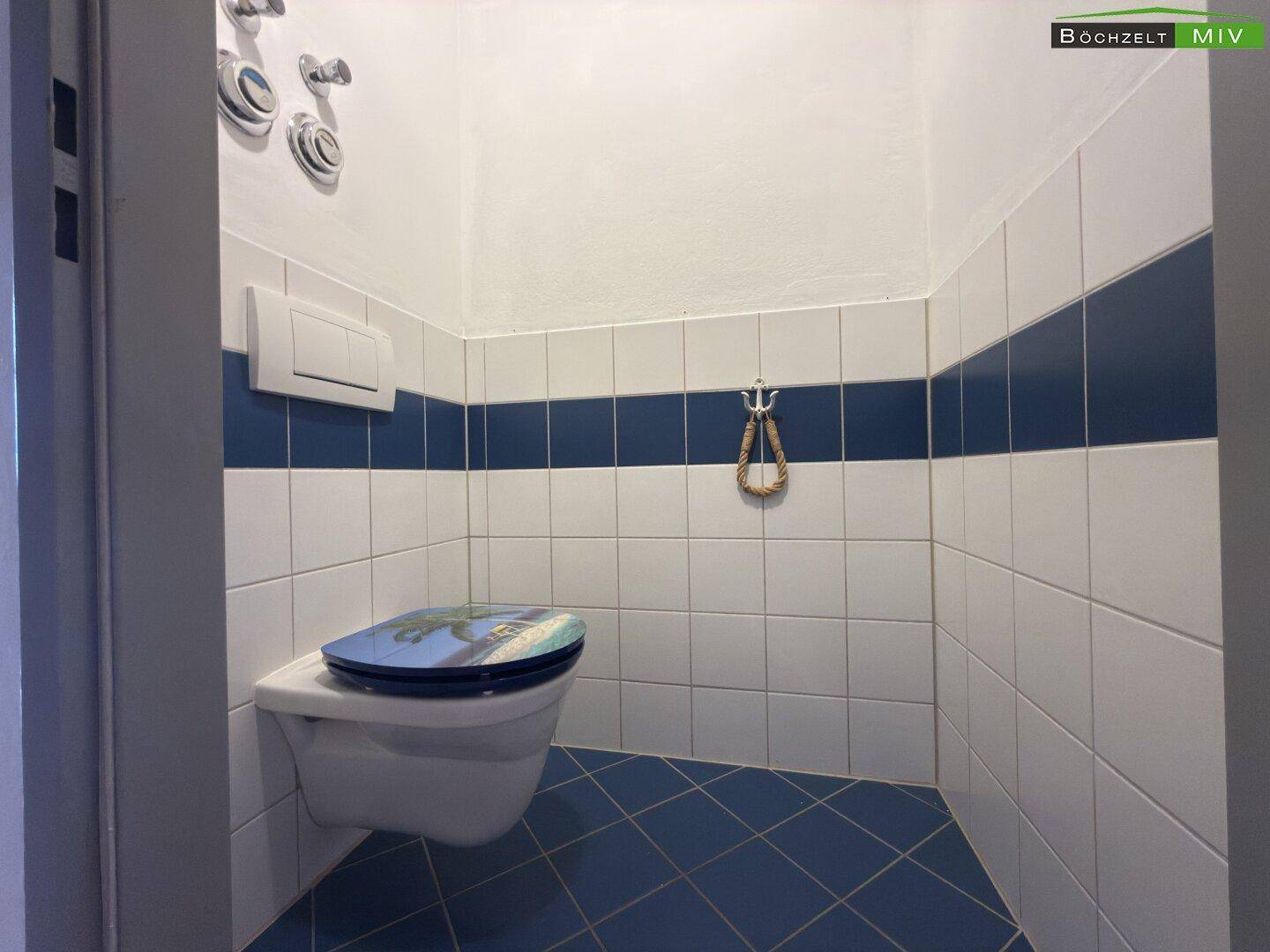 Kleines Gäste-WC mit blauen und weißen Fliesen sowie einer Wandtoilette.