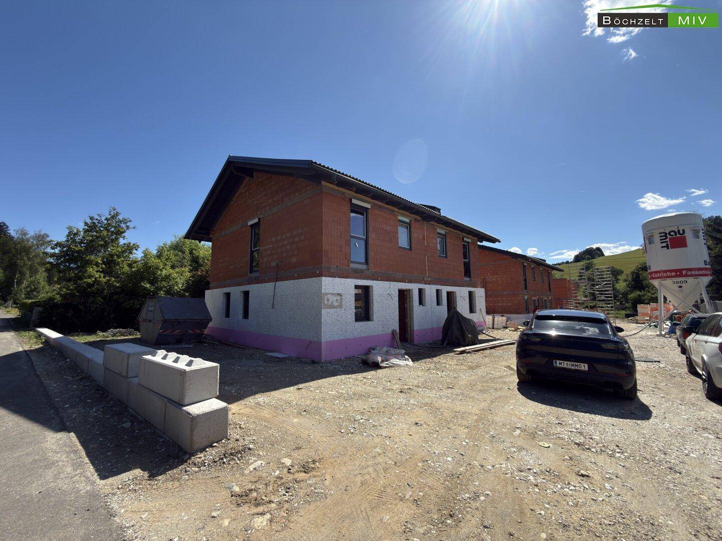 Panoramablick auf das im Bau befindliche Haus mit umliegender Natur und weiteren Baustellenaktivitäten.