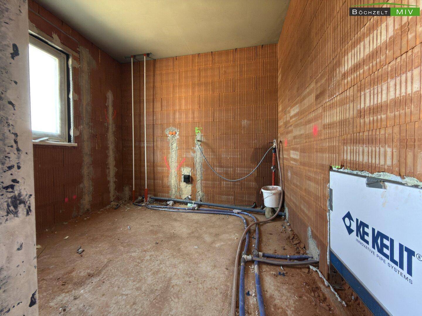 Badezimmer im Rohbau mit Fenster, vorbereiteten Anschlüssen für Sanitäranlagen und unverputzten Wänden.