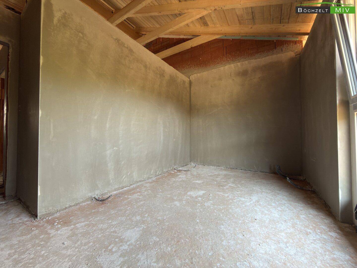 Ecke eines Dachgeschosszimmers im Rohbau mit schrägen Wänden und sichtbarer Holzkonstruktion des Daches.