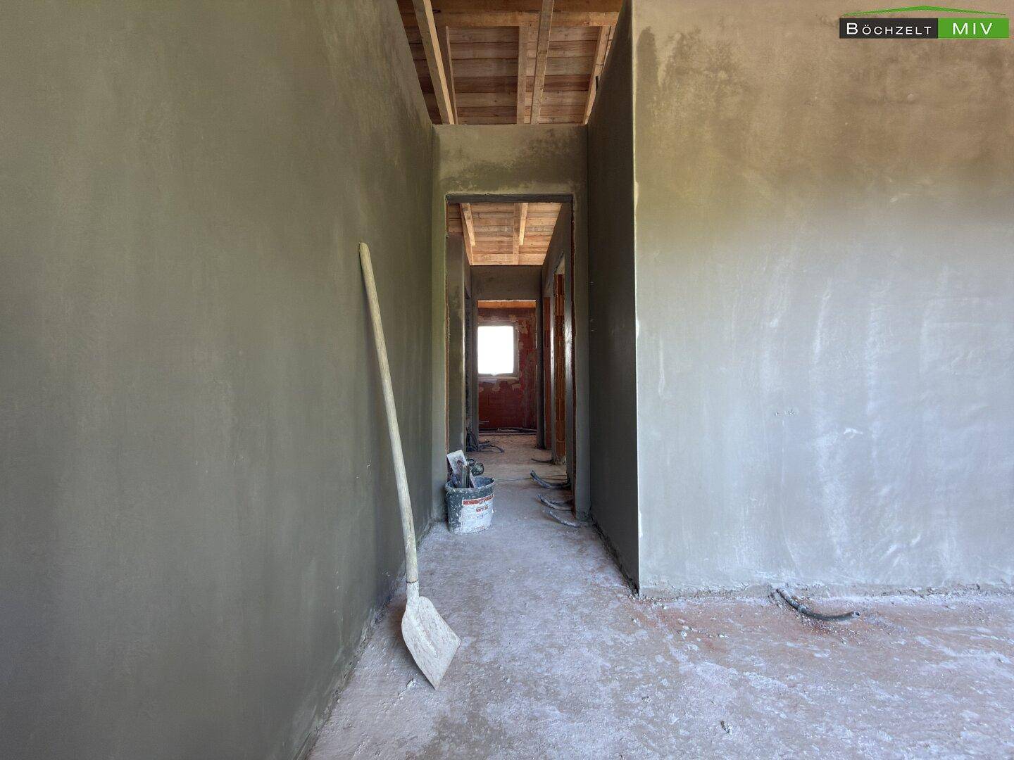 Flur im Obergeschoss des Rohbaus mit verputzten Wänden und sichtbarer Holzkonstruktion des Daches.
