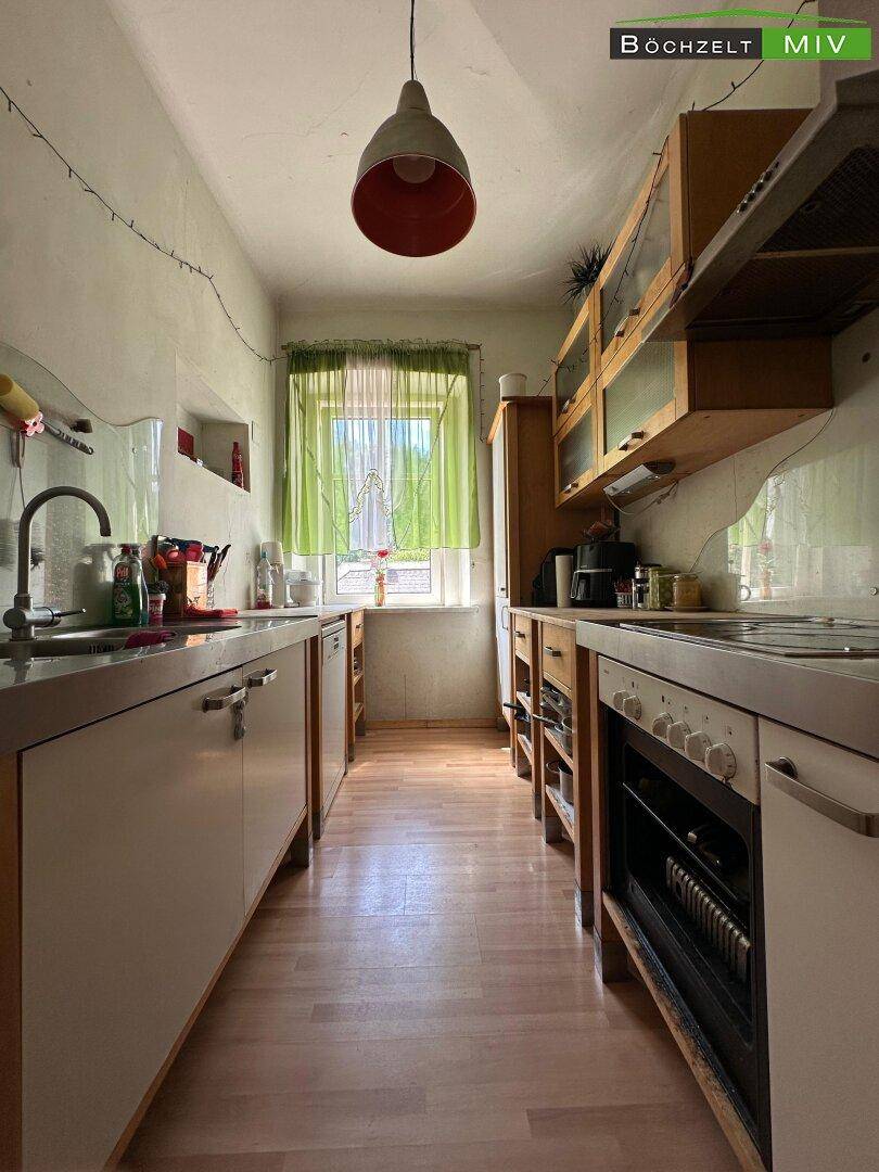 Schmale Küche mit Holzschränken, Edelstahlspüle und einem Fenster.