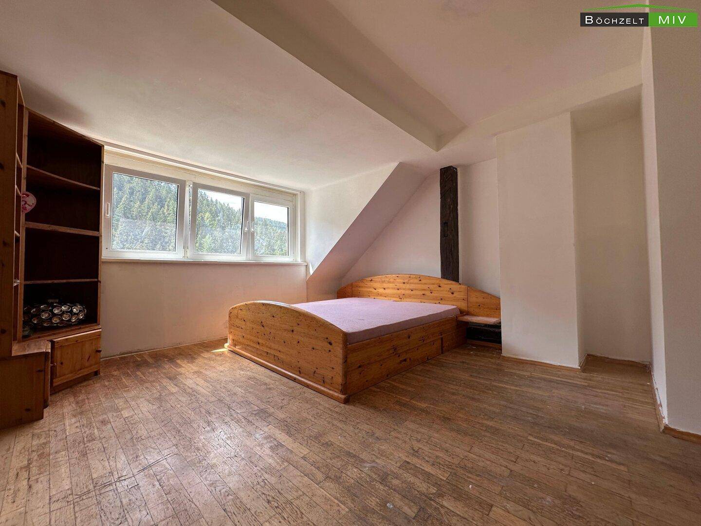 Schlafzimmer mit Holzboden, Dachschräge und einem Bett unter den Fenstern.