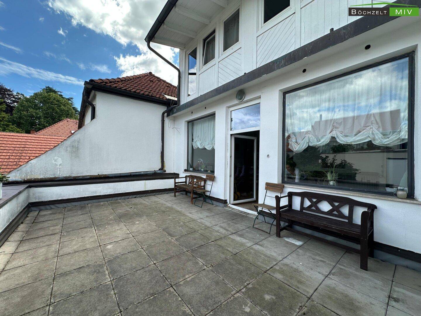 Weitläufige Außenterrasse mit Steinplatten und Zugang zum Haus durch eine Glastür.