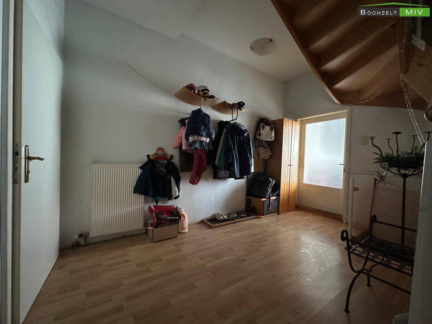Eingangsbereich mit Holzboden, Heizkörper und Garderobe unter einer Treppe.