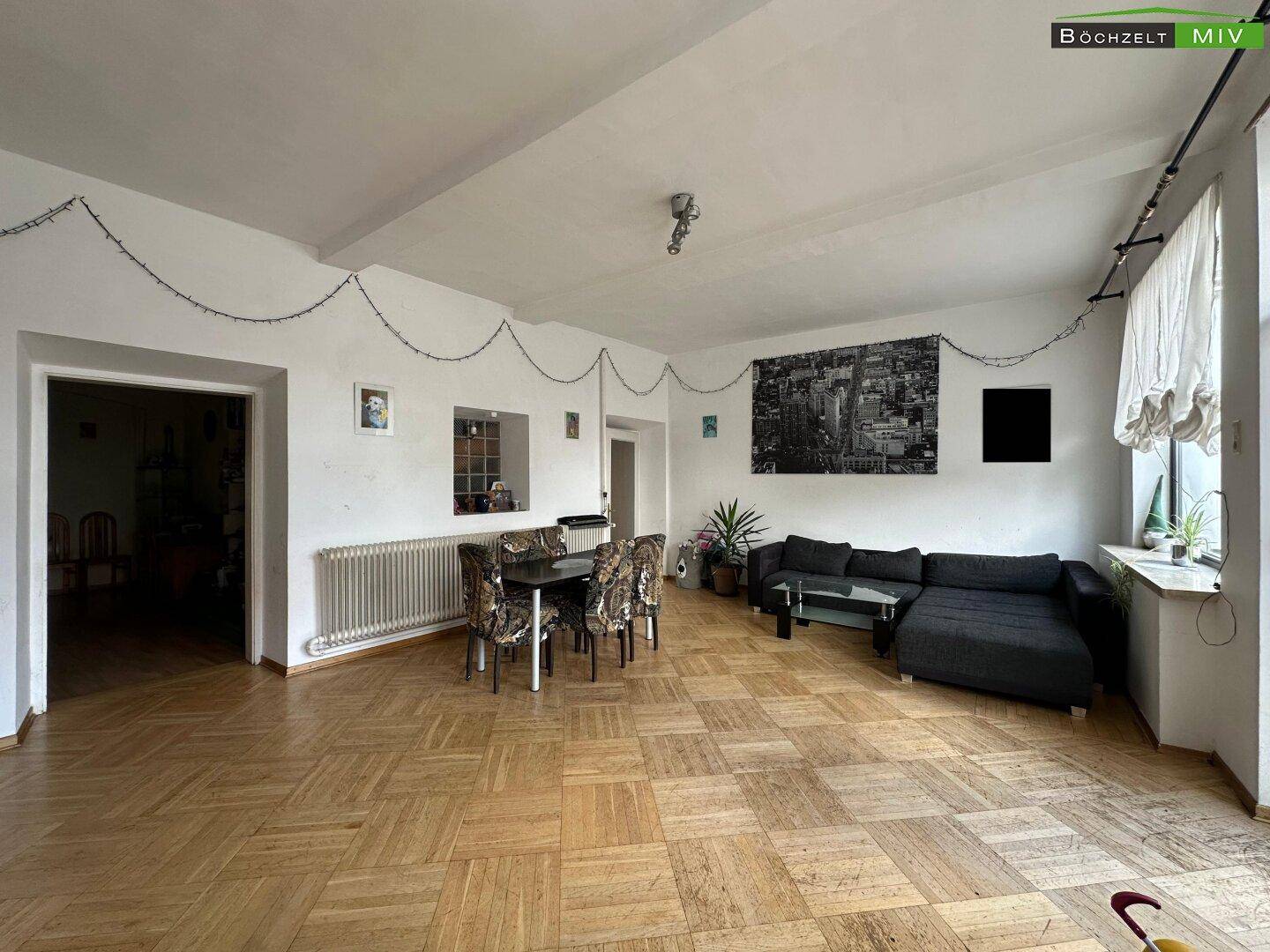 Heller Wohn- und Essbereich mit Parkettboden, großem Sofa und Esstisch.