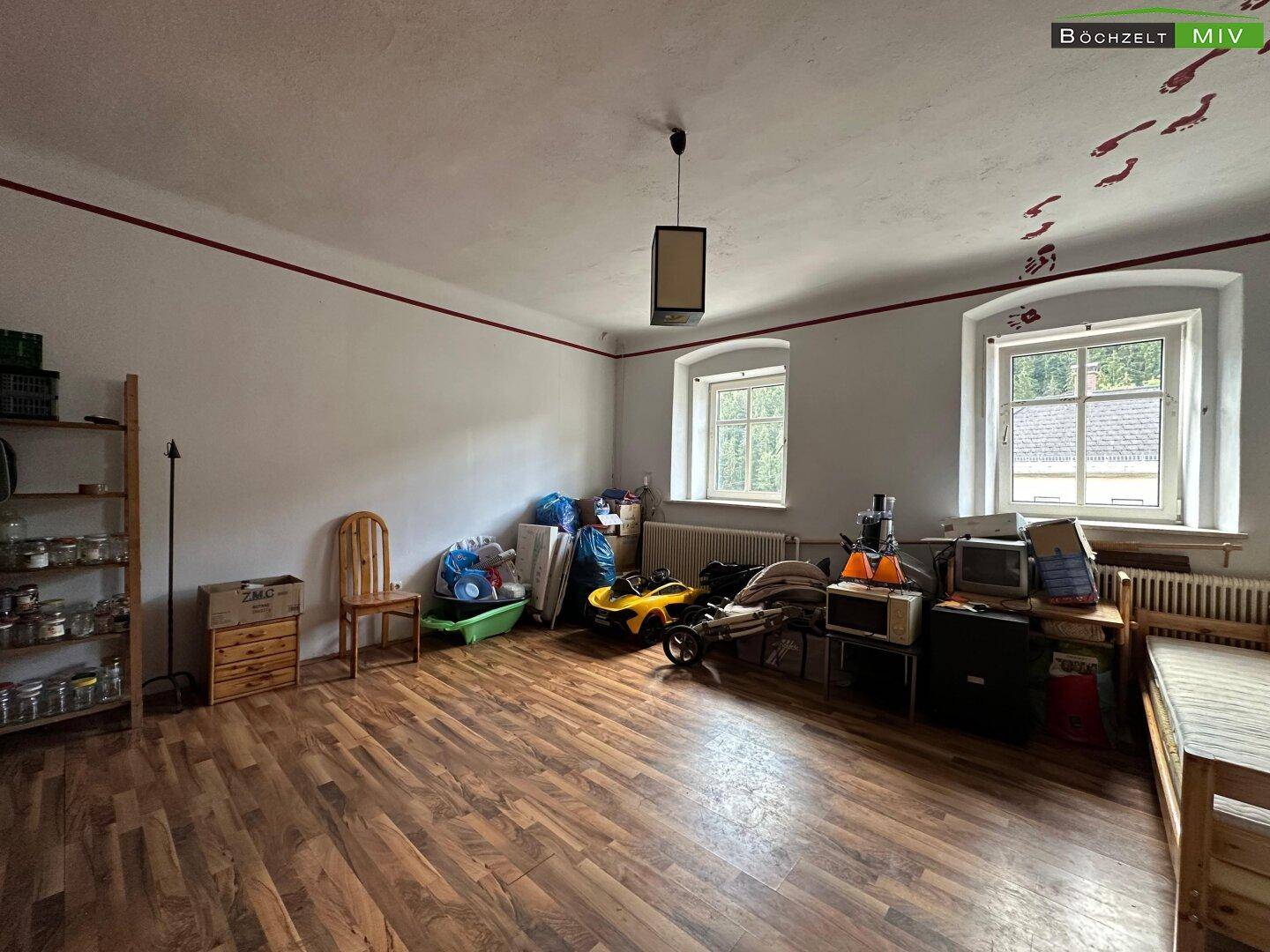 Geräumiger Raum mit Holzboden, zwei Fenstern und verschiedenen Gegenständen gelagert.