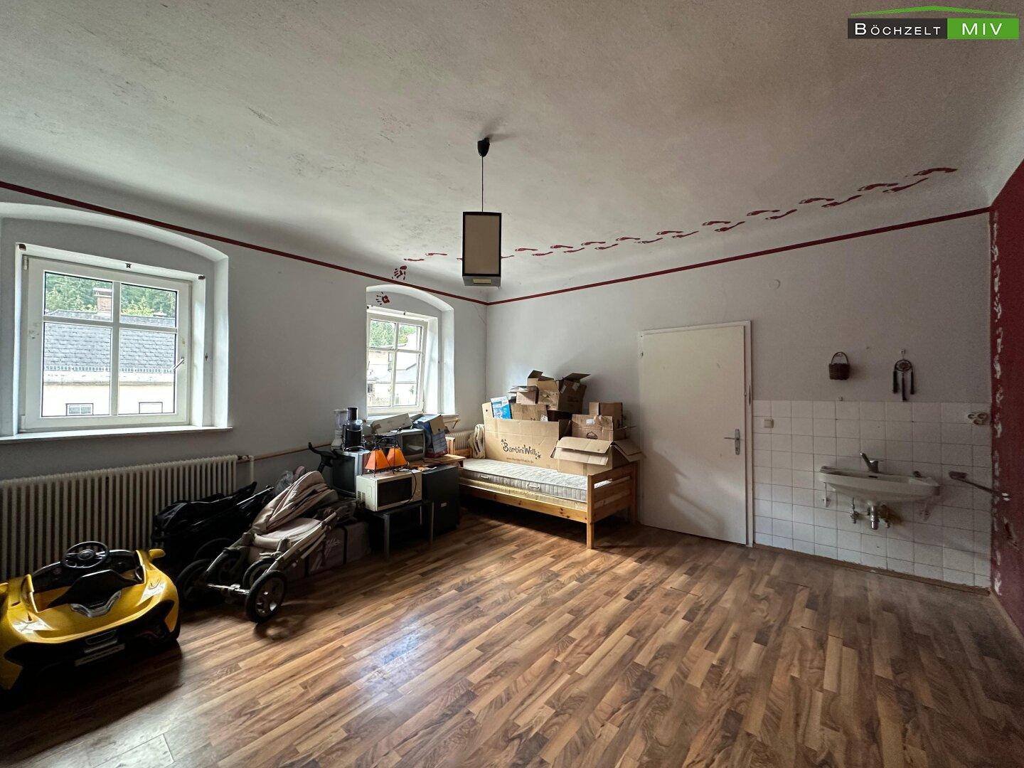 Großer Raum mit Holzboden, Heizkörpern und einem Waschbecken an der Wand.