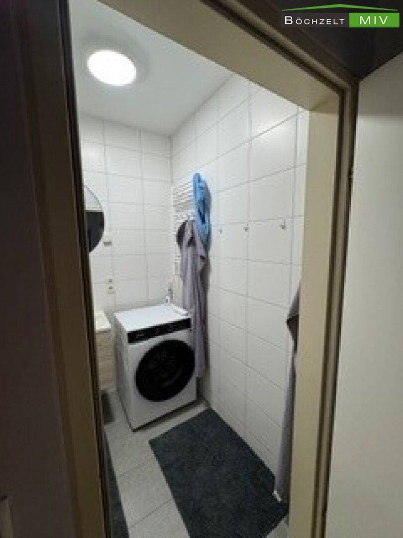 Badezimmer mit Waschmaschine, Handtuchhalter und hellen Fliesen.