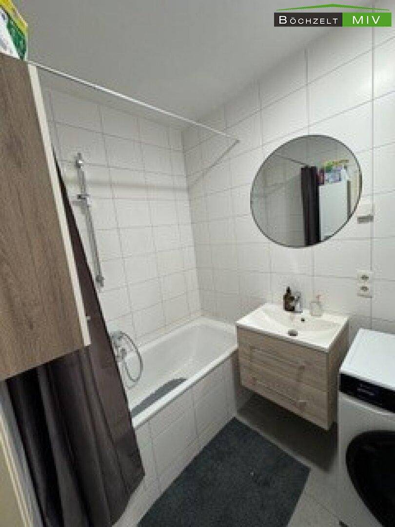 Modernes Badezimmer mit Badewanne, Waschbecken, Spiegel und Waschmaschine.
