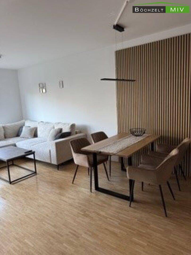 Offener Wohn-Essbereich mit modernem Esstisch, bequemer Couch und dekorativer Holzwand.