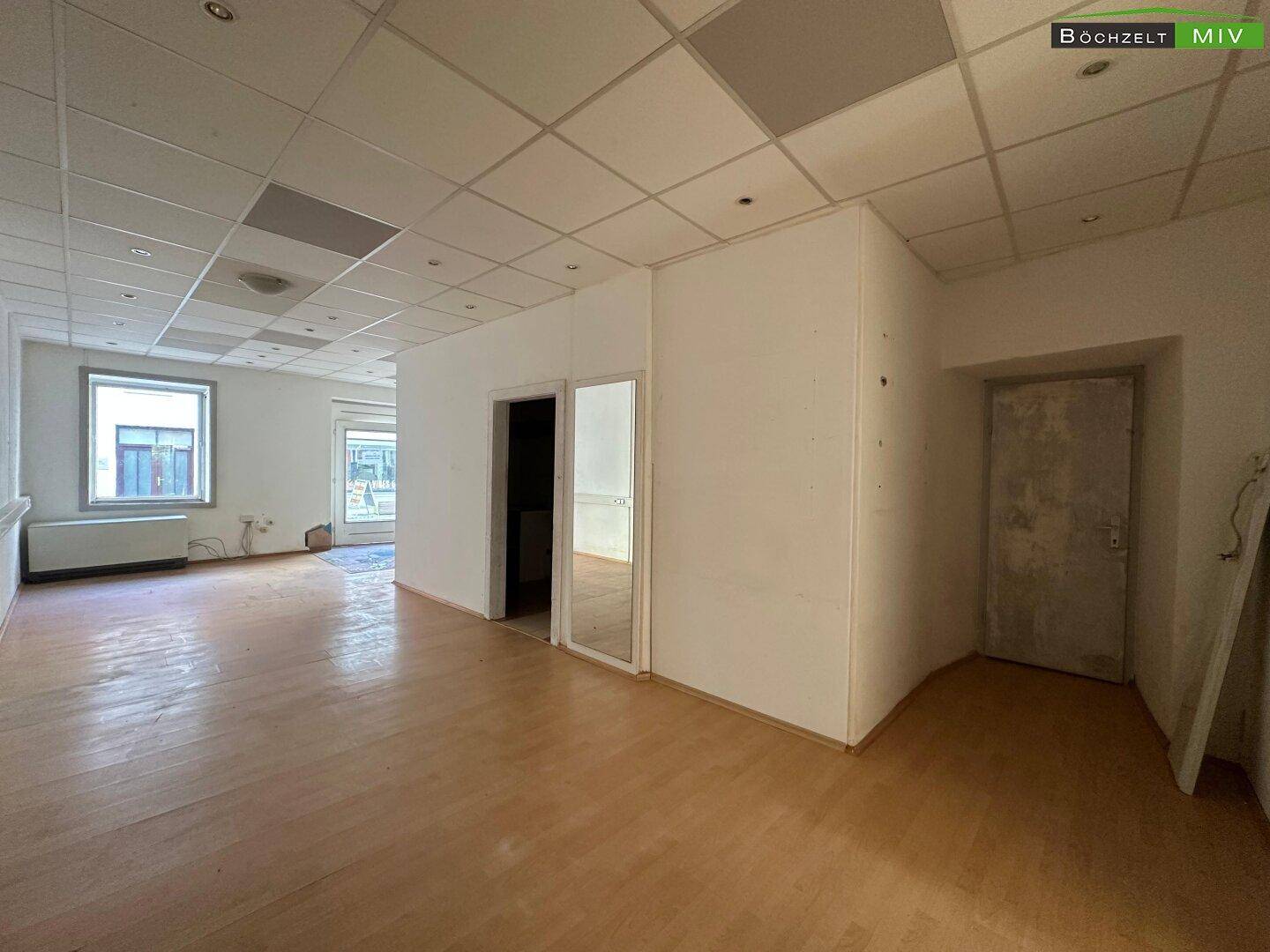 Heller Gewerberaum mit Laminatboden, abgehängter Decke und einem Fenster, das Tageslicht hereinlässt.