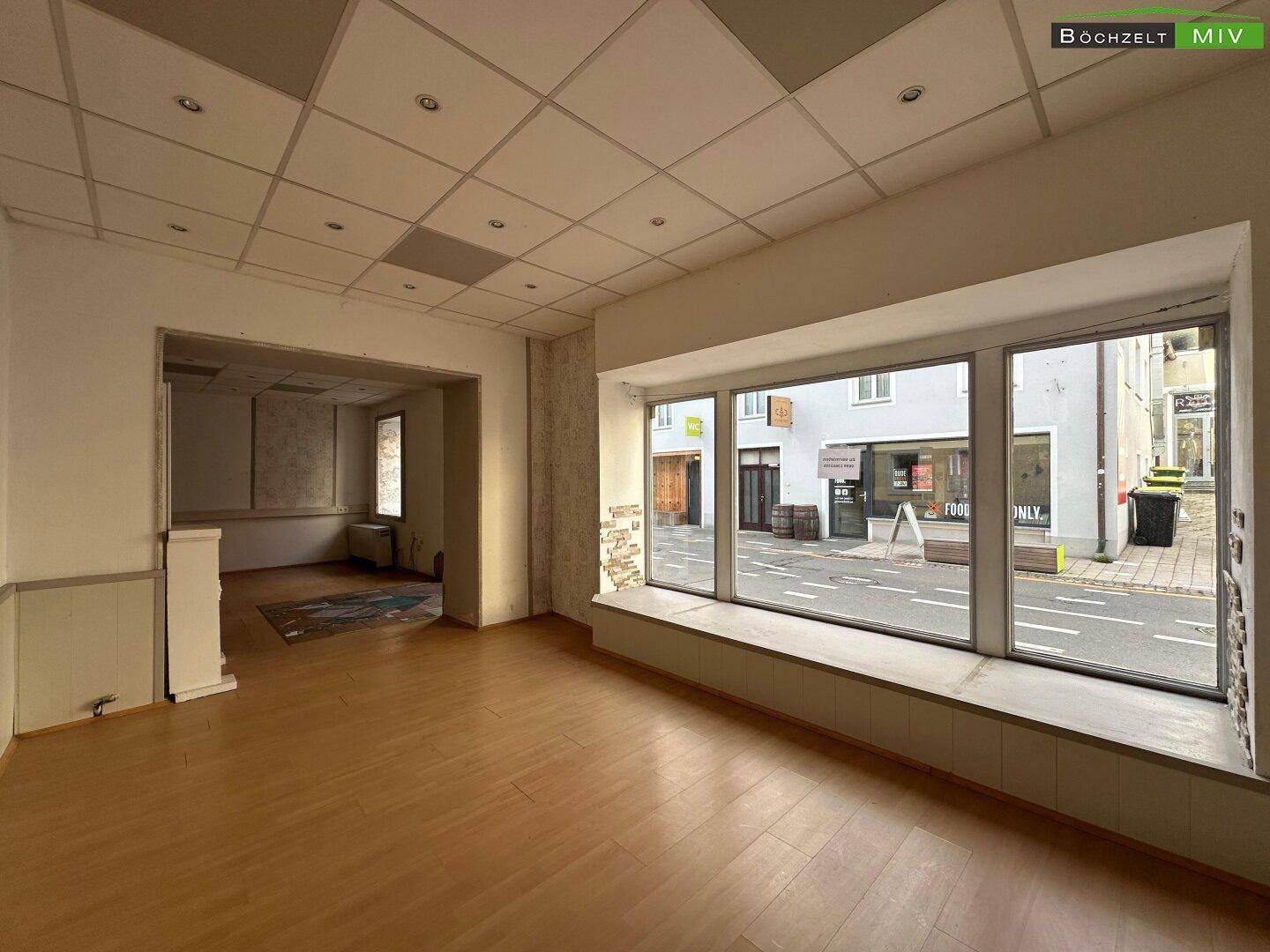 Geräumiger Gewerberaum mit Laminatboden, großen Schaufenstern und Blick auf die belebte Straße.