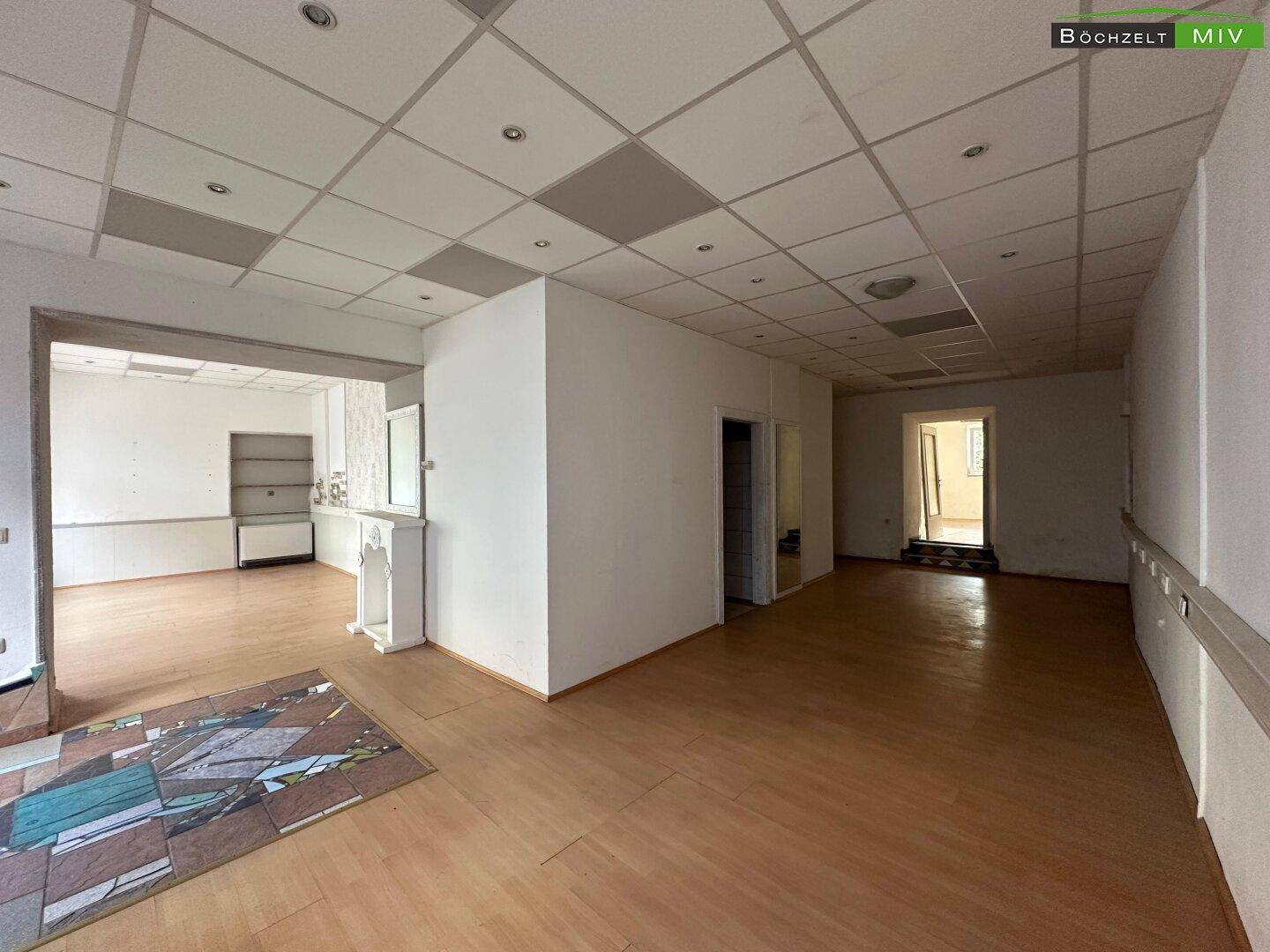Großzügiger Gewerberaum mit Laminatboden, abgehängter Decke und einem dekorativen Kaminsims als Akzent.