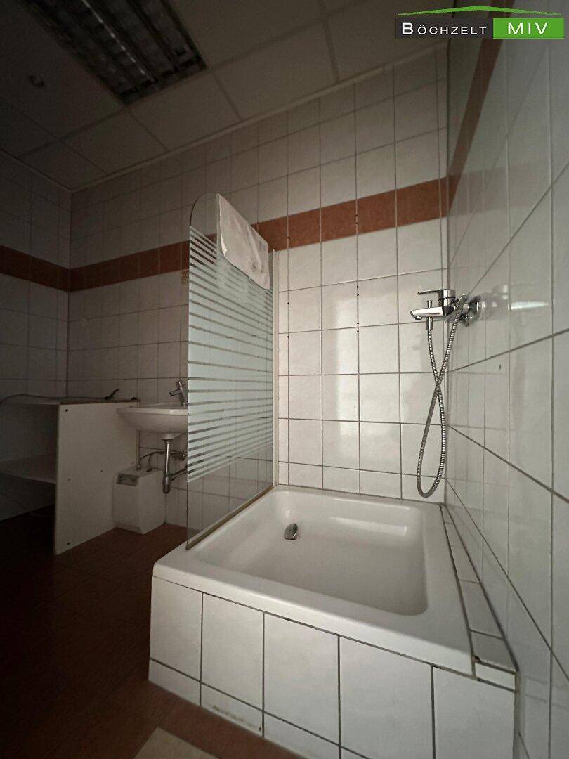 Badezimmer mit Badewanne, integrierter Dusche und weißen Fliesen an den Wänden und dem Boden.