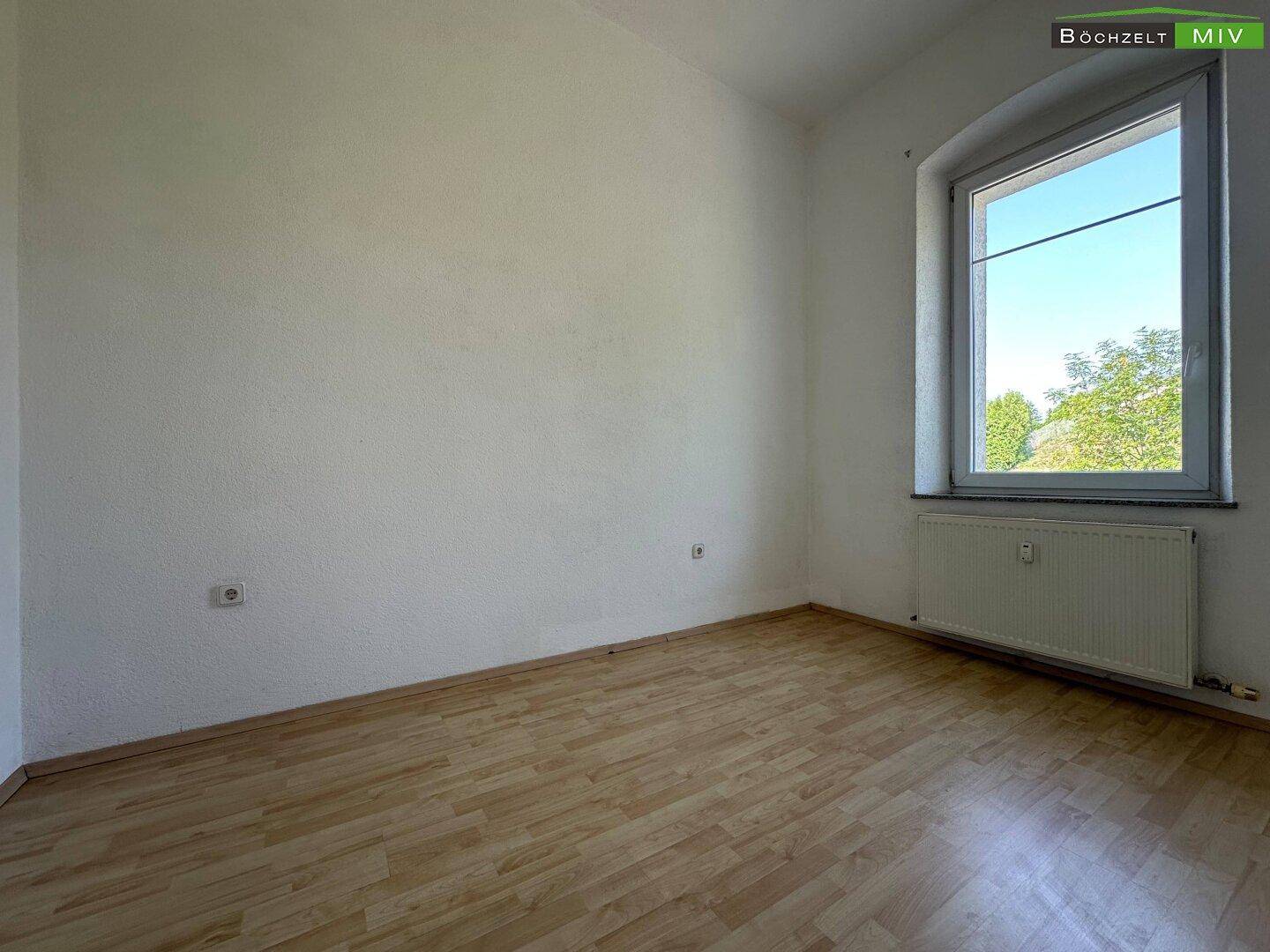 Freundliches Zimmer mit hellem Laminatboden und einem Fenster, das viel Tageslicht hereinlässt.