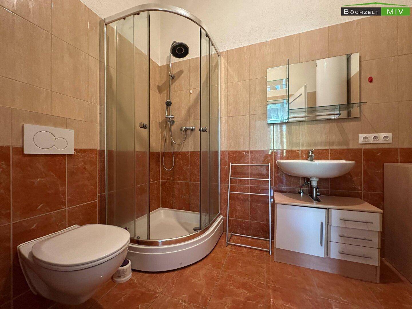 Badezimmer mit braunen Fliesen, Eckdusche, wandhängendem WC und Waschtisch mit Spiegelschrank.