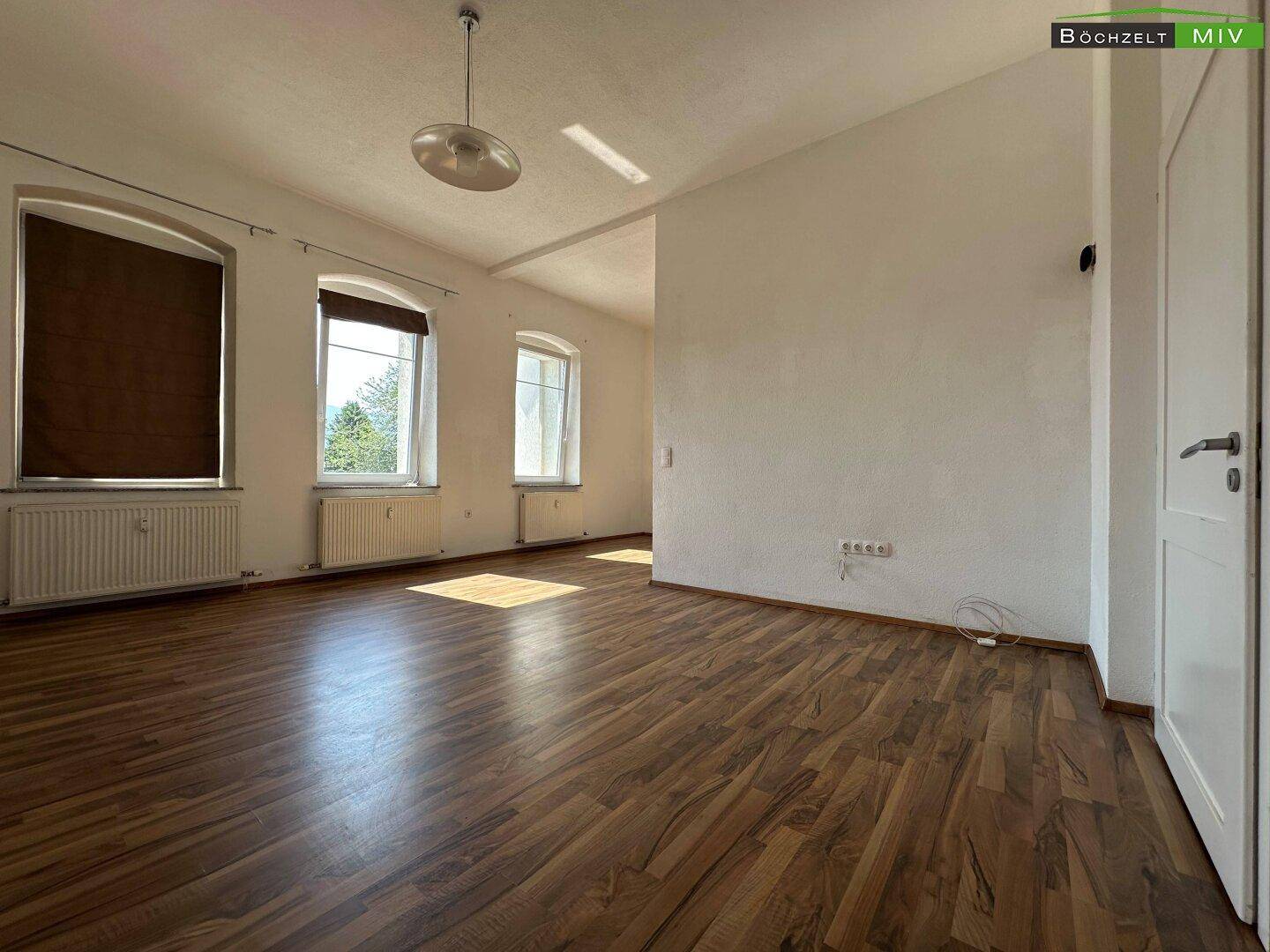 Geräumiger Wohnbereich mit Laminatboden, großen Fenstern und einem schönen Blick ins Grüne.