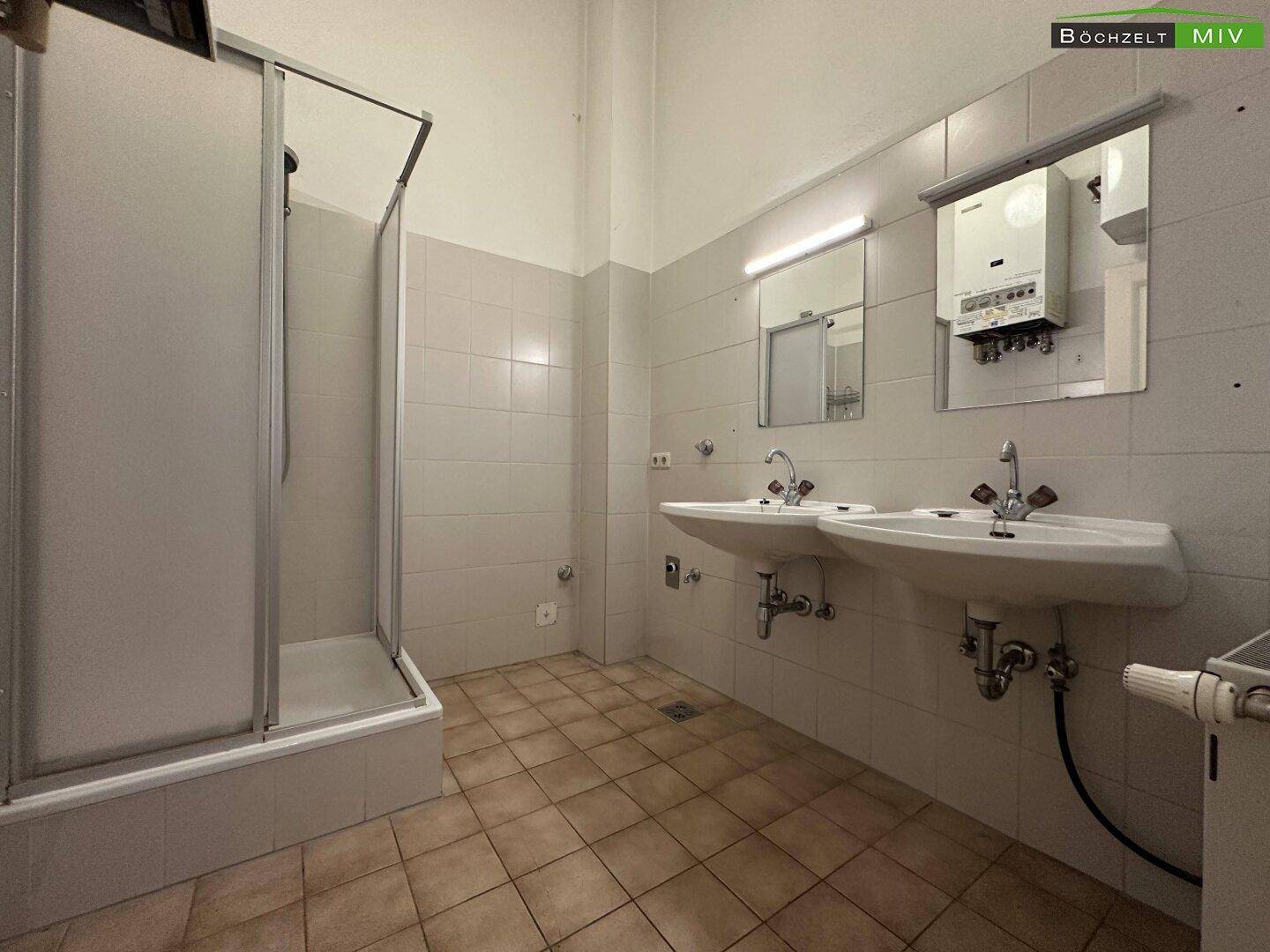Badezimmer mit zwei Waschbecken, Duschkabine und hellen Fliesen an Wänden und Boden.