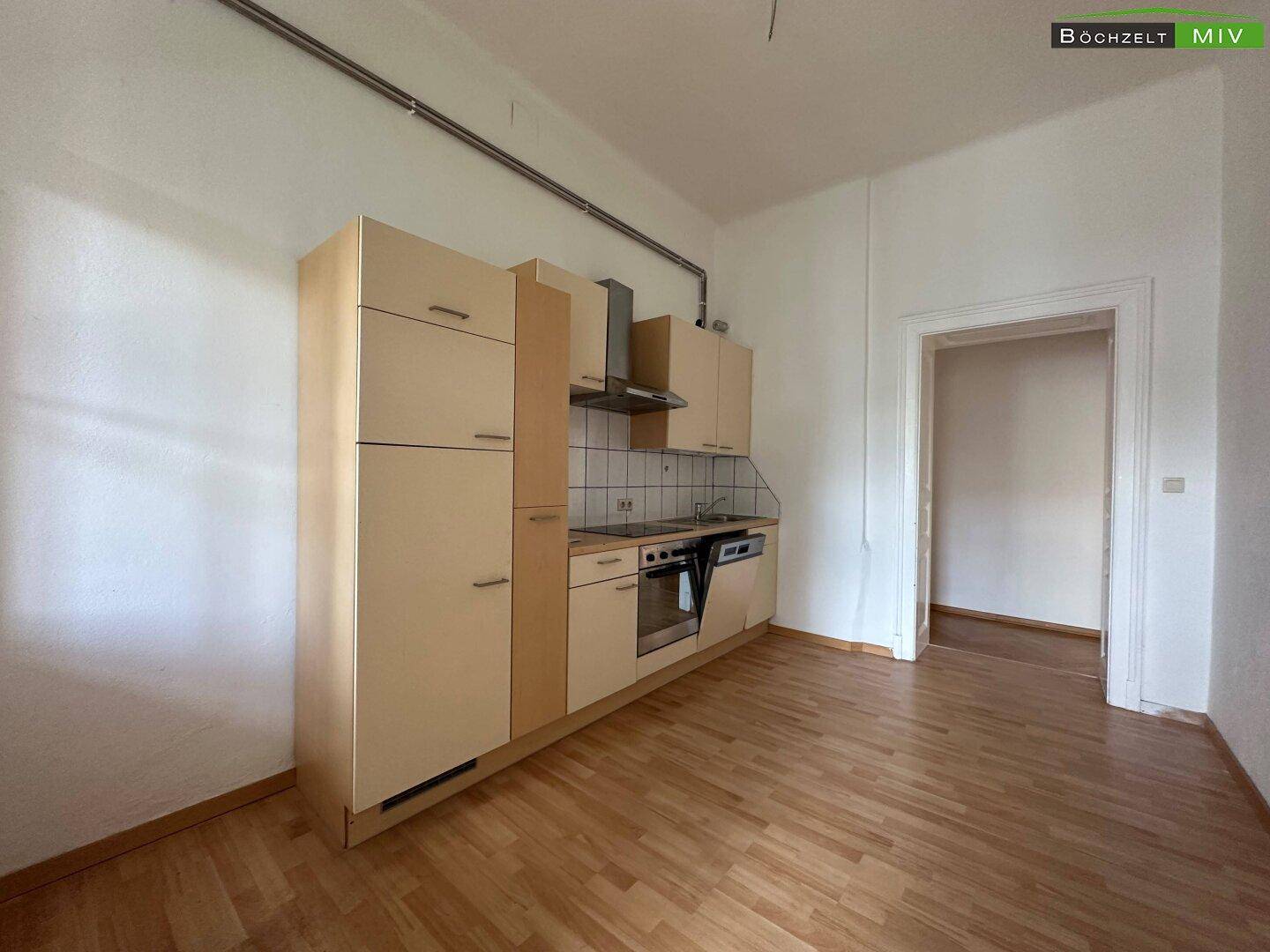 Einfache Einbauküche mit hellen Schränken und Parkettboden in einem leeren Raum.