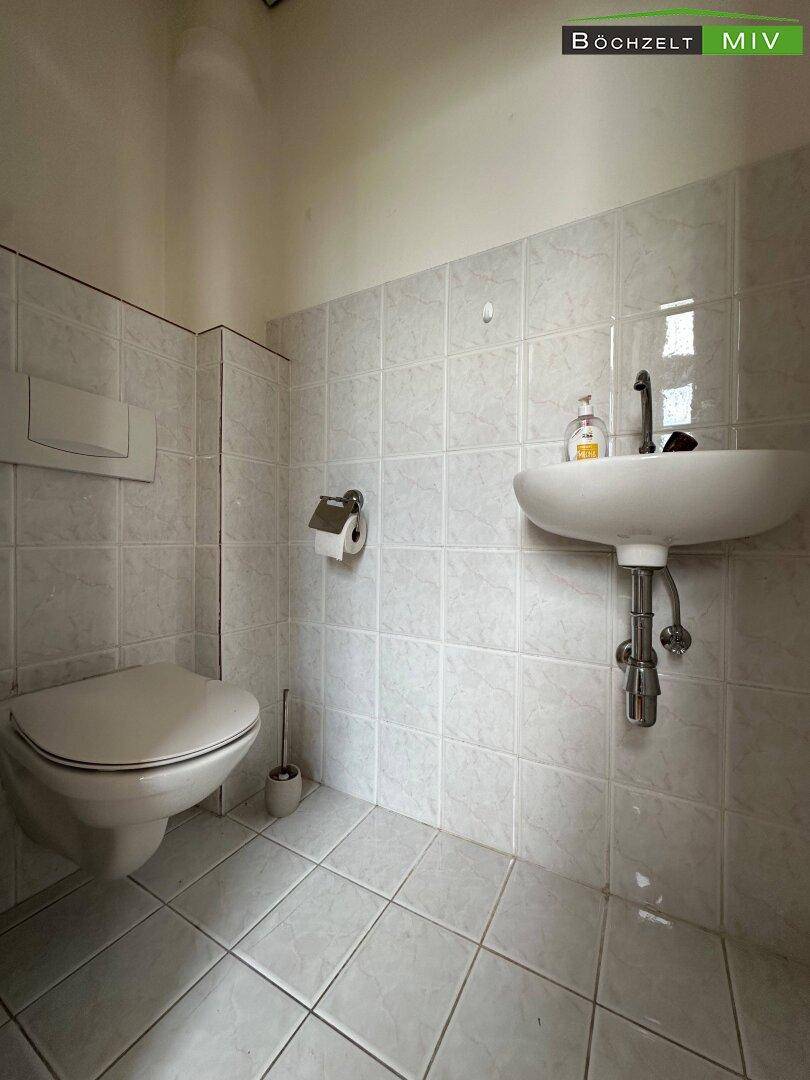 Kleines Gäste-WC mit Wand-WC, Waschbecken und hellen Fliesen an Wänden und Boden.