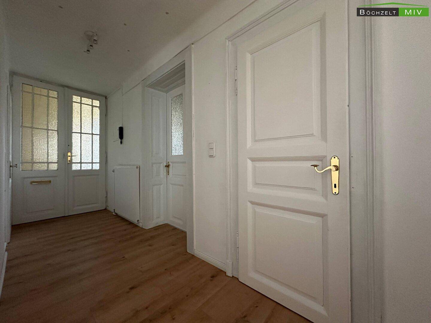 Flur mit Laminatboden und mehreren weißen Holztüren, die zu den Zimmern führen.