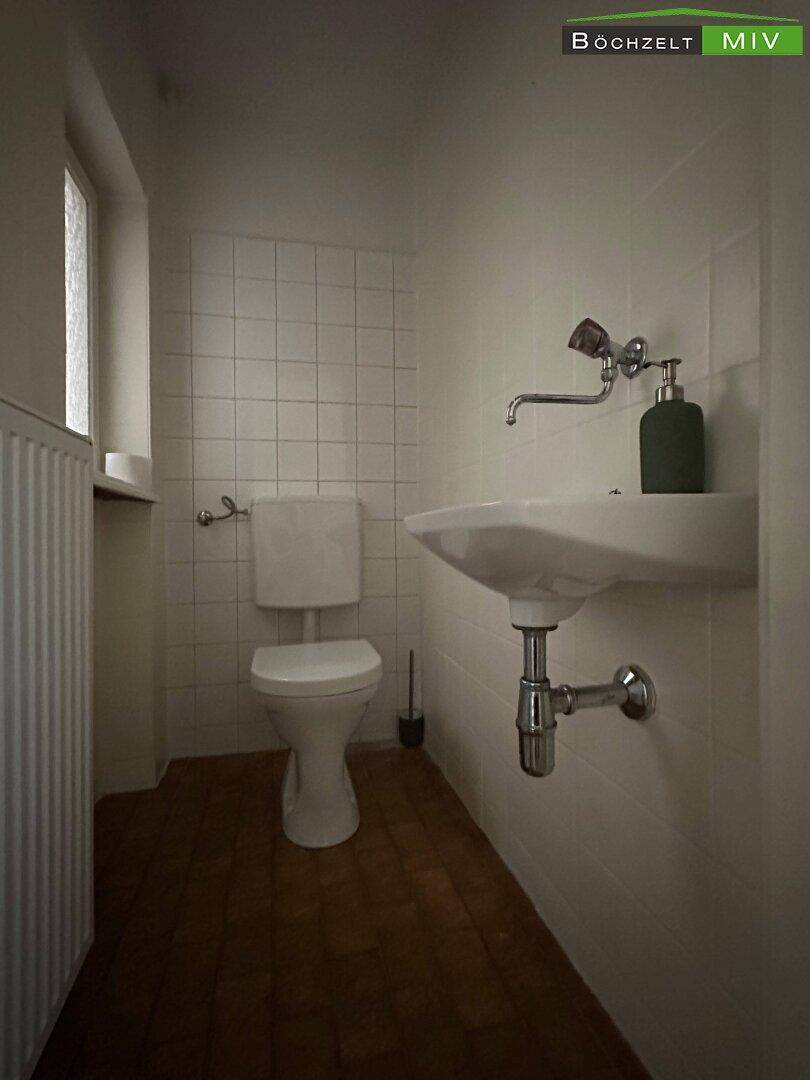 Kleines Gäste-WC mit weißen Fliesen, Waschbecken und Toilette.