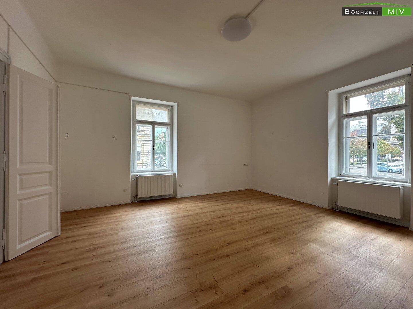 Großes, helles Zimmer mit Laminatboden und zwei Fenstern zur Straße.