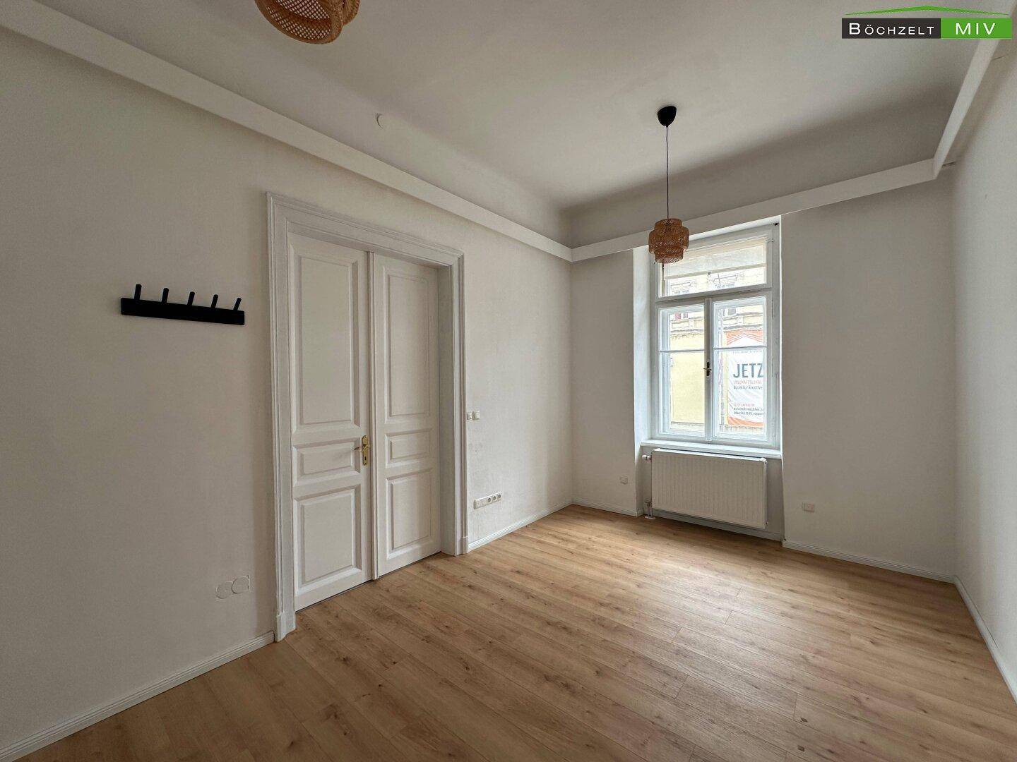 Helles Zimmer mit Laminatboden, hohen Decken und einer klassischen Doppeltür.