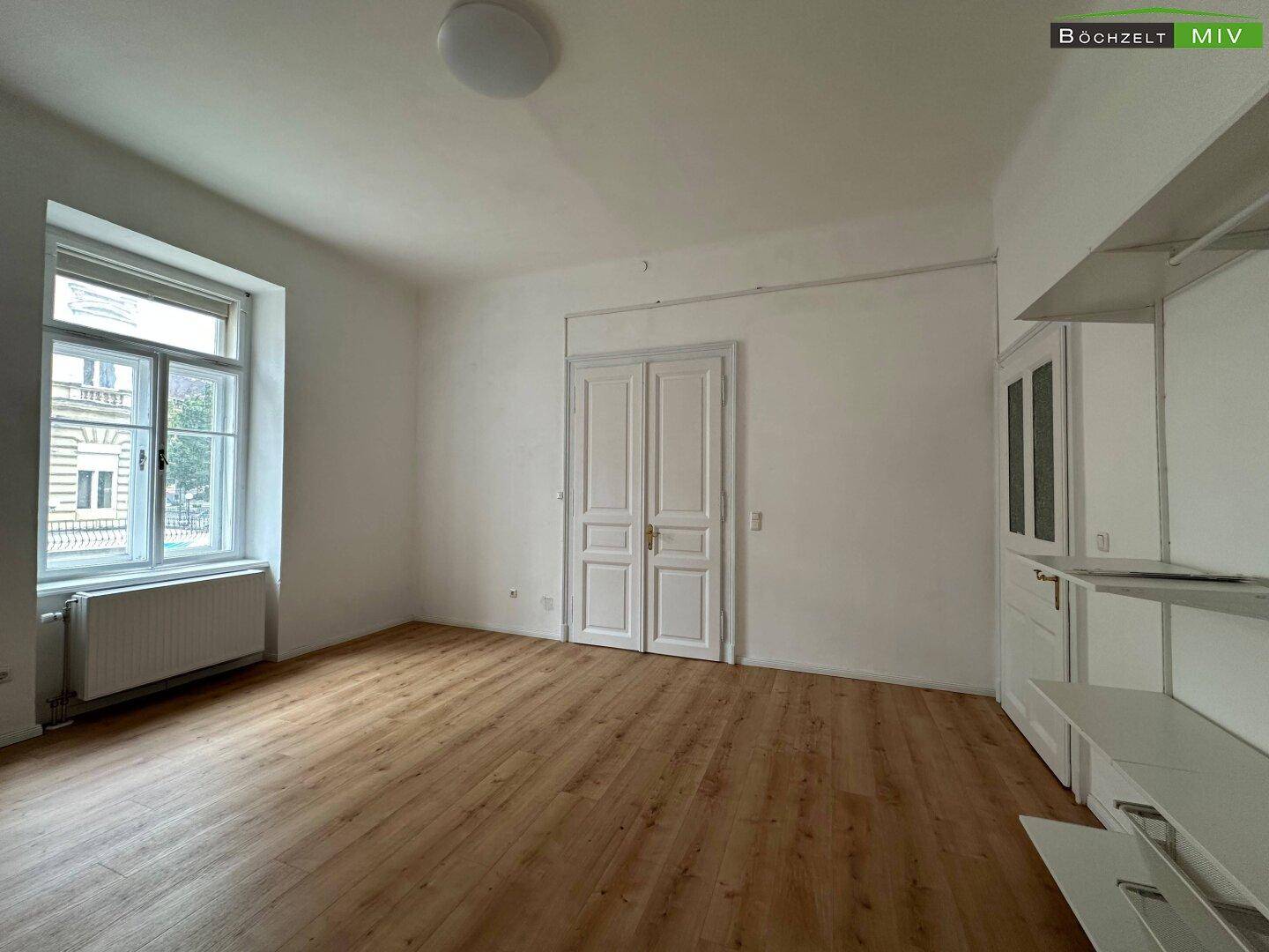 Heller Wohnbereich mit Laminatboden und einem kleinen Küchenelement an der Wand.