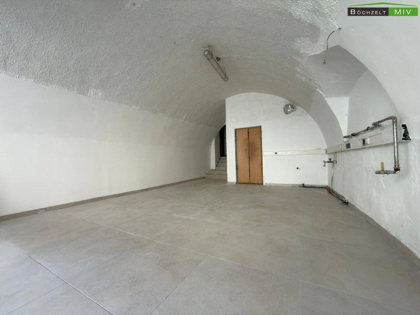 Geräumiger Innenraum mit gewölbter Decke, Fliesenboden und sichtbaren Installationen an der Wand.