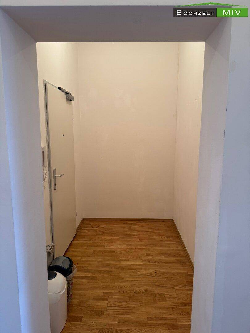 Heller Eingangsbereich mit Holzboden und weißer Tür, der zu den weiteren Räumen führt.