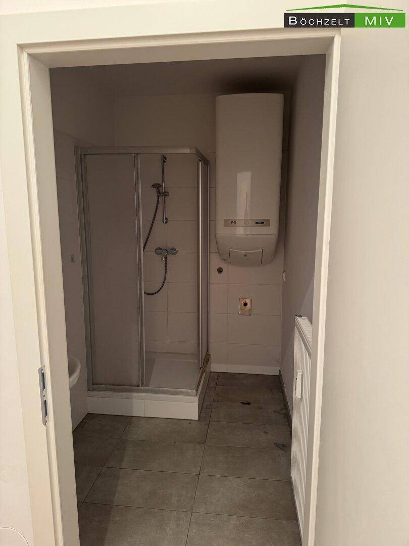 Badezimmer mit Duschkabine und Warmwasserboiler, ausgestattet mit modernen Fliesen.