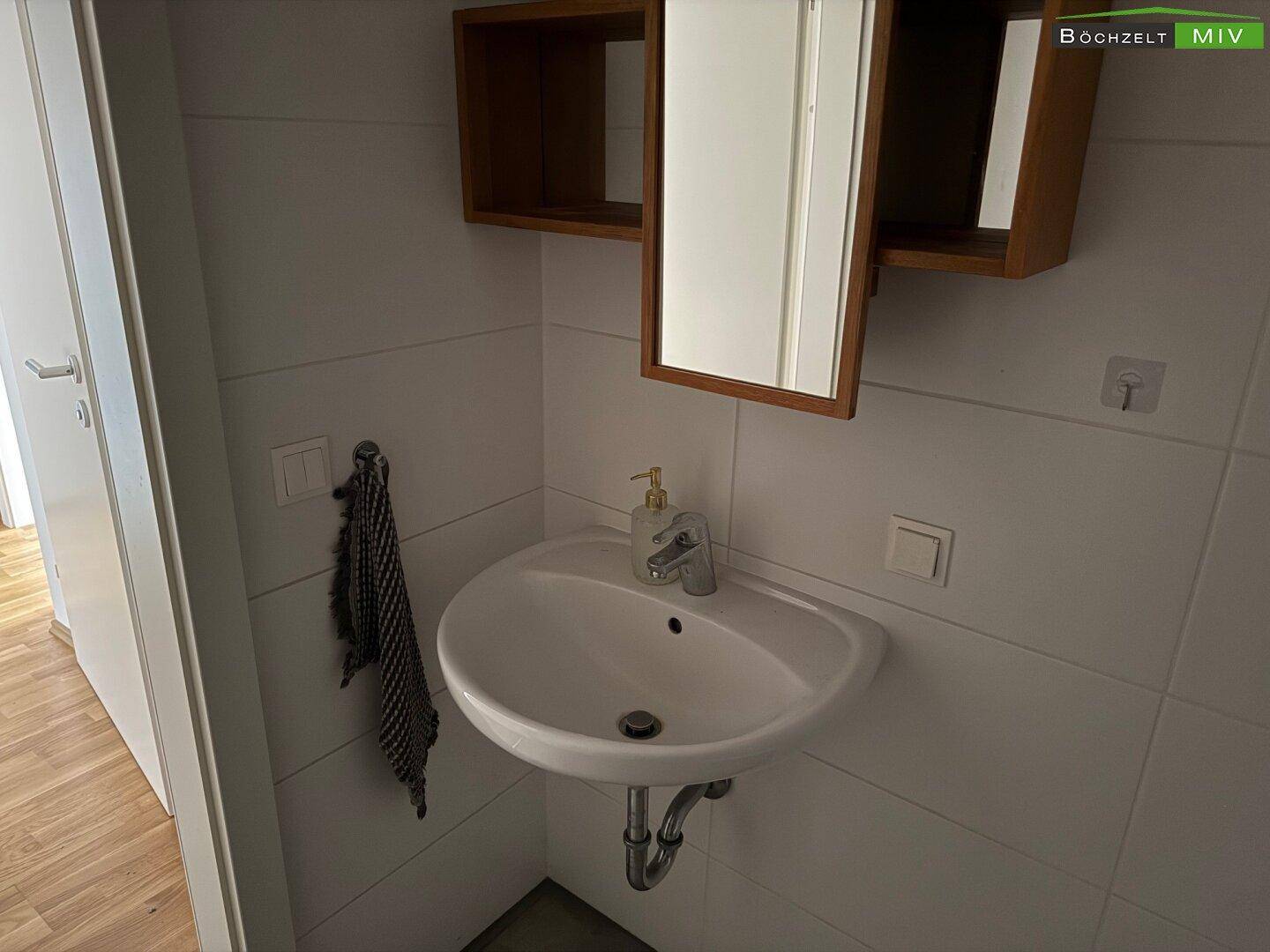 Badezimmer mit modernem Waschbecken und Spiegelschrank, umgeben von hellen Fliesen.