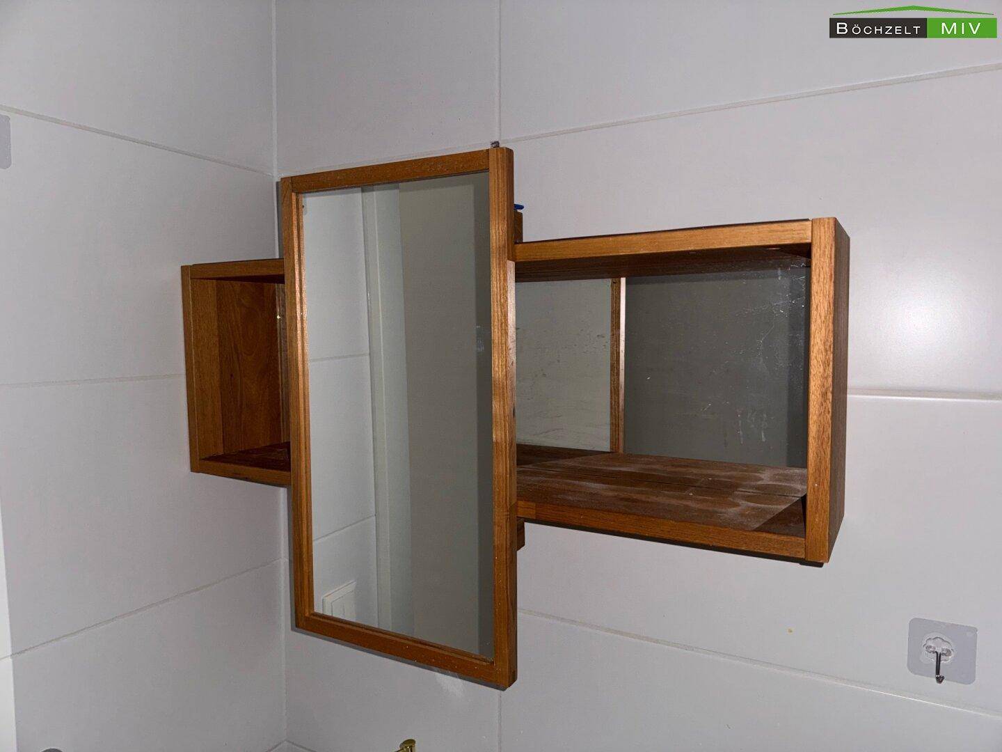 Detailaufnahme eines hölzernen Spiegelschranks mit integrierten Ablageflächen im Badezimmer.