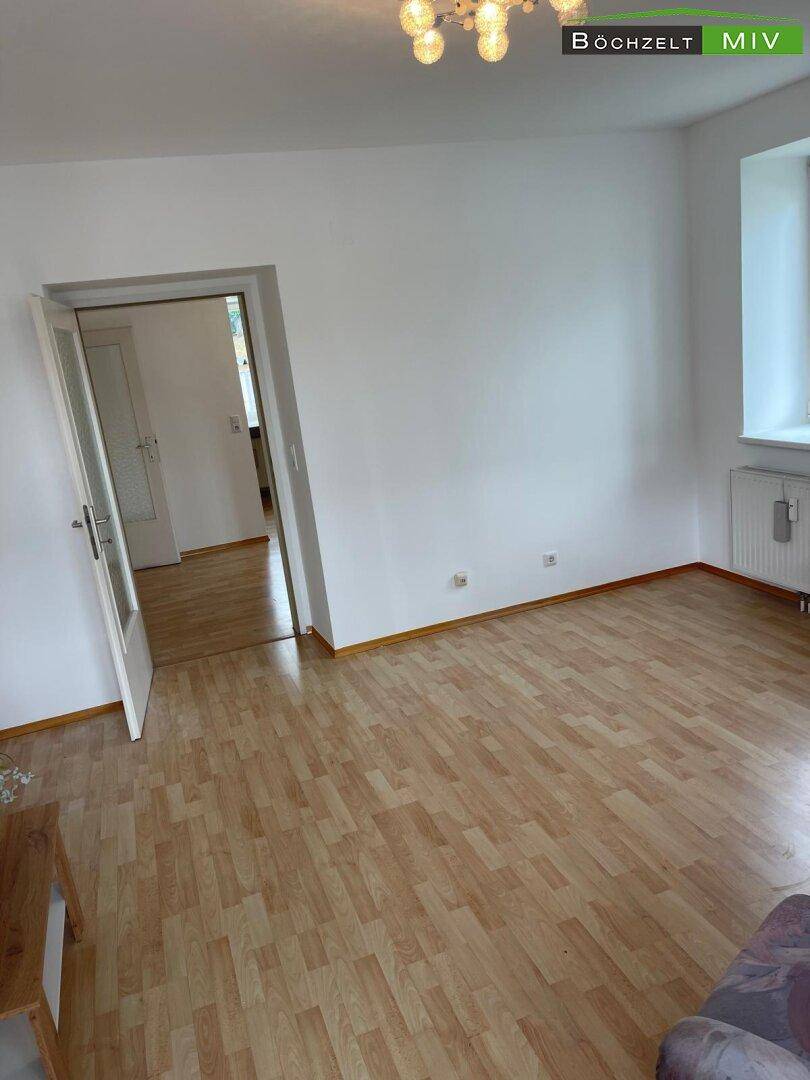 Geräumiger, heller Raum mit Laminatboden und Zugang zu einem weiteren Zimmer, vielseitig nutzbar.