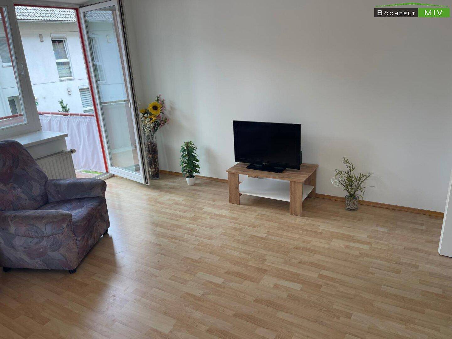 Wohnzimmer mit Laminatboden, Zugang zum Balkon und Blick auf die umliegenden Gebäude.
