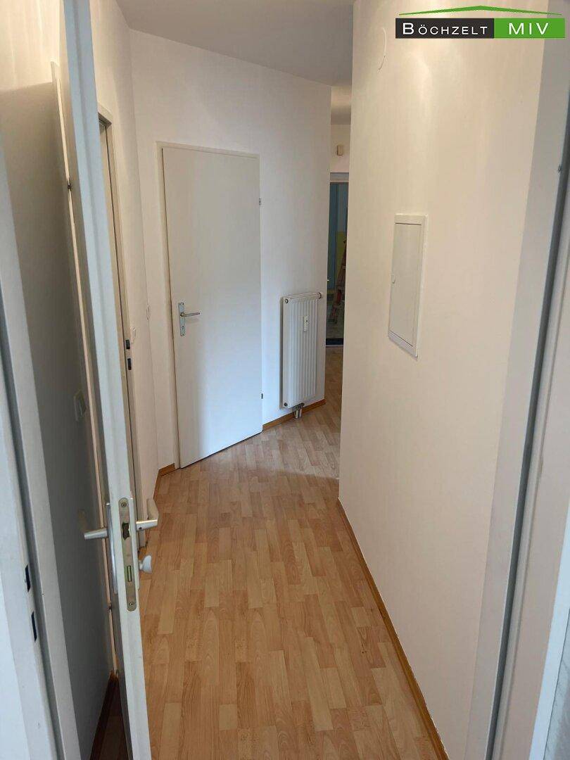 Langer, heller Flur mit Laminatboden und Heizkörper, der verschiedene Bereiche der Wohnung verbindet.
