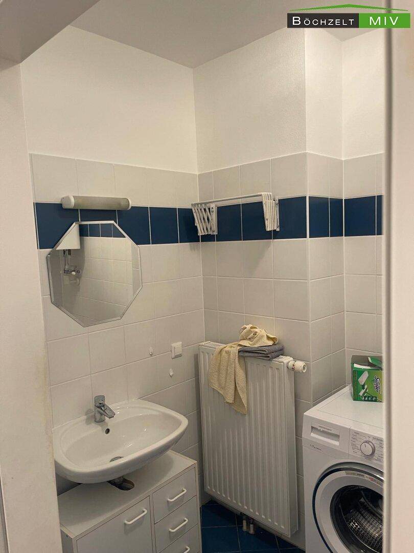 Badezimmer mit Waschbecken, Spiegel und Waschmaschine, gefliest in Weiß und Blau.