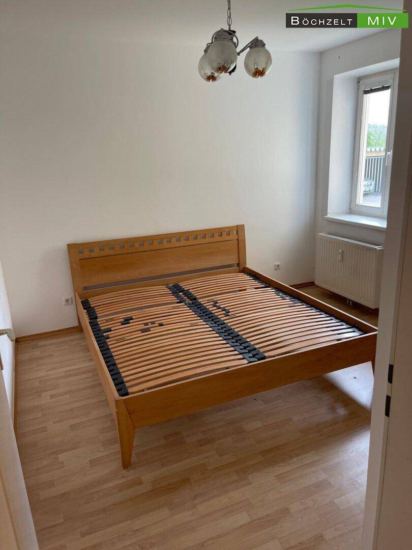 Schlafzimmer mit hellem Holzbettrahmen und Laminatboden, bereit zur individuellen Gestaltung.