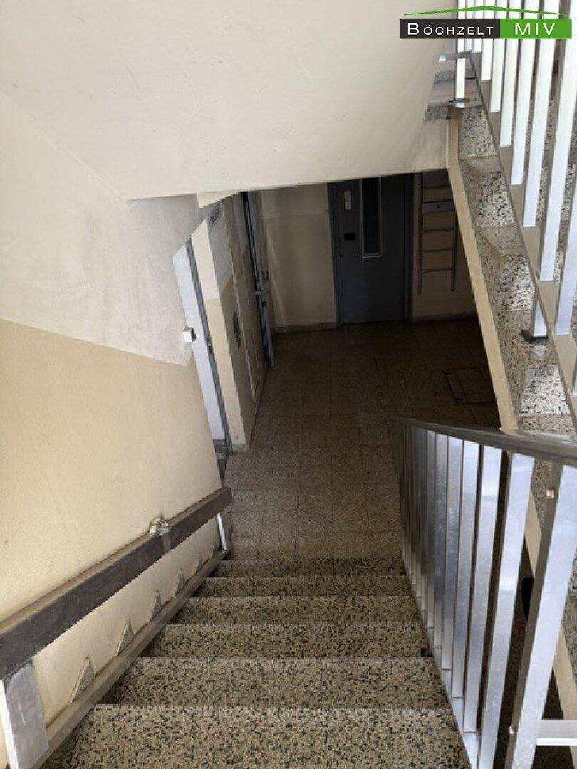Treppenhaus mit Terrazzostufen und Metallgeländer, das in die unteren Stockwerke führt.