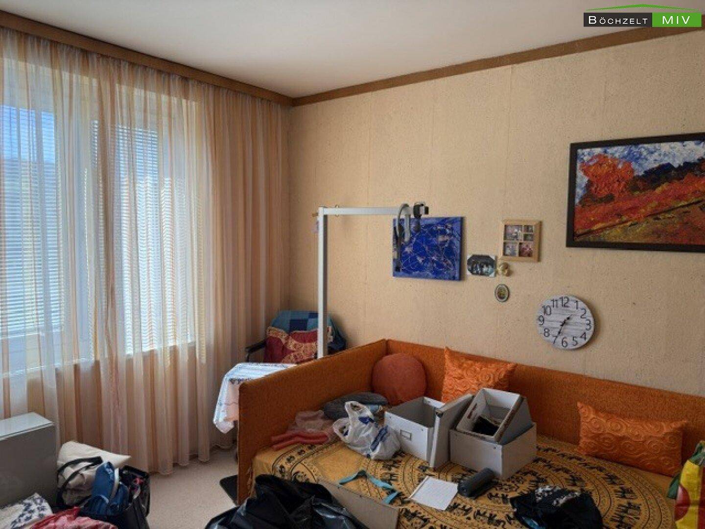 Helles Schlafzimmer mit Einzelbett, Vorhängen und einfacher Einrichtung.