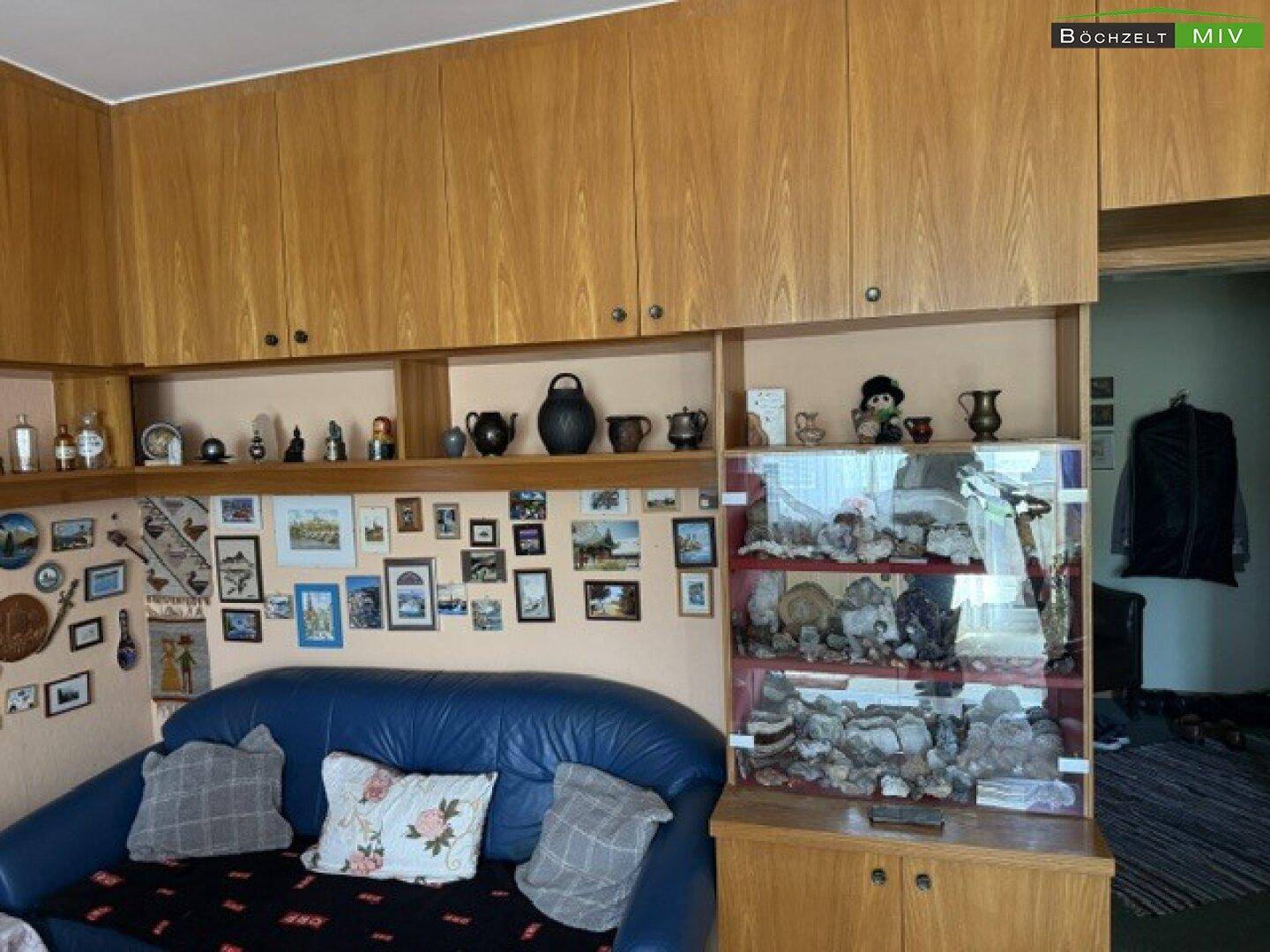 Wohnzimmer mit blauer Couch, Holzschränken und vielen persönlichen Dekorationen.