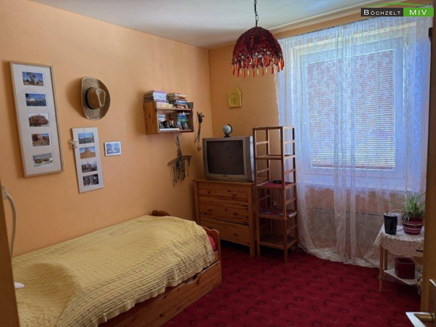 Gemütliches Schlafzimmer mit rotem Teppichboden, Einzelbett und Fenster.