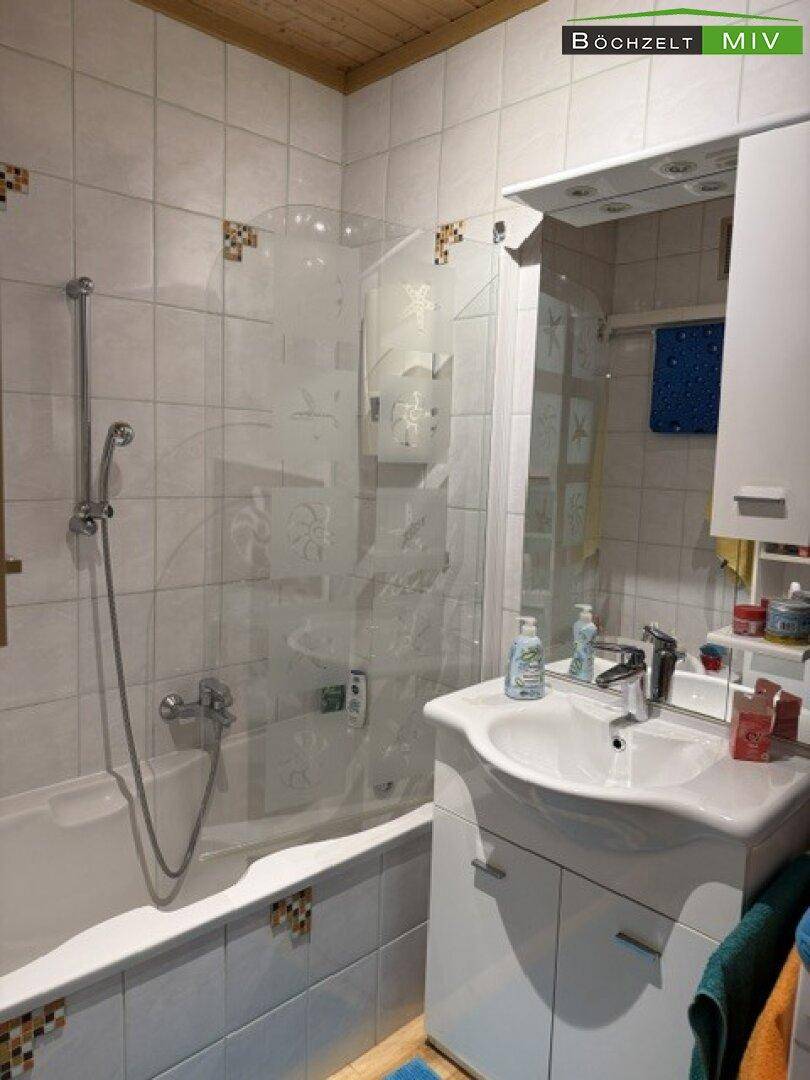 Gefliestes Badezimmer mit Badewanne, Duschabtrennung und Waschbecken mit Spiegelschrank.